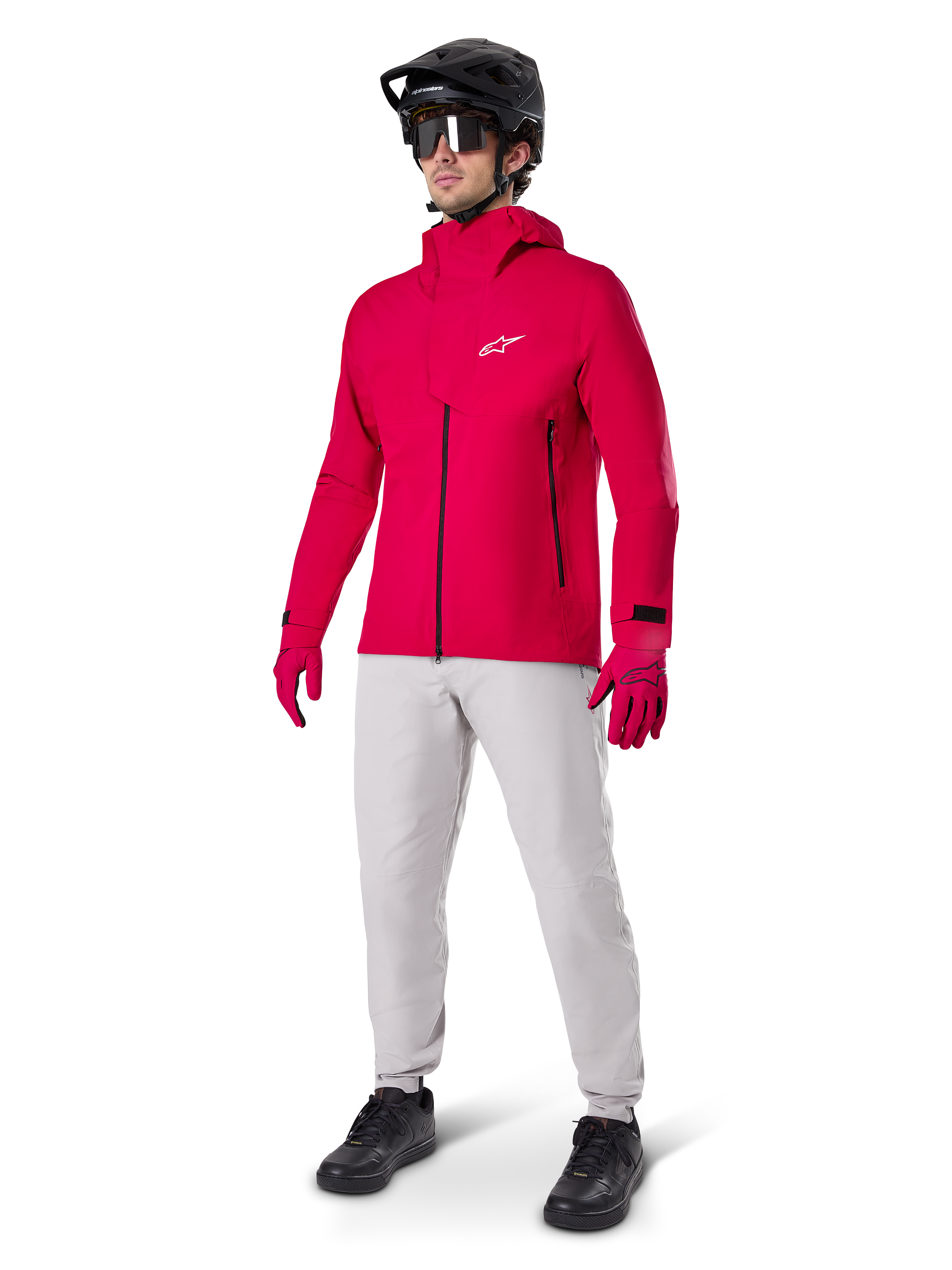 Model ubrany w spodnie Alpinestars A-Dura Waterproof w kolorze Titanium gray, zestawione z jaskrawoczerwoną wodoodporną kurtką i pasującymi rękawicami, czarny kask MTB z goglami oraz czarne buty, kompletny strój na rower górski na mokre warunki na szlaku