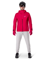 Spodnie Alpinestars A-Dura Waterproof, spodnie MTB, kolor Titanium Gray, noszone z jasnoczerwoną kurtką z kapturem, czerwonymi rękawicami i czarnym kaskiem rowerowym MTB, profesjonalna wodoodporna odzież rowerowa na mokre warunki na szlaku