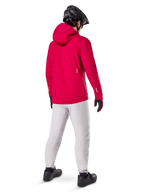Alpinestars A-Dura Waterproof Pants w kolorze Titanium, widok z tyłu na rowerzystę w jasnoszarych technicznych spodniach MTB, jaskrawoczerwona kurtka z kapturem i czarny kask, wytrzymała wodoodporna odzież na rower w mokrych warunkach