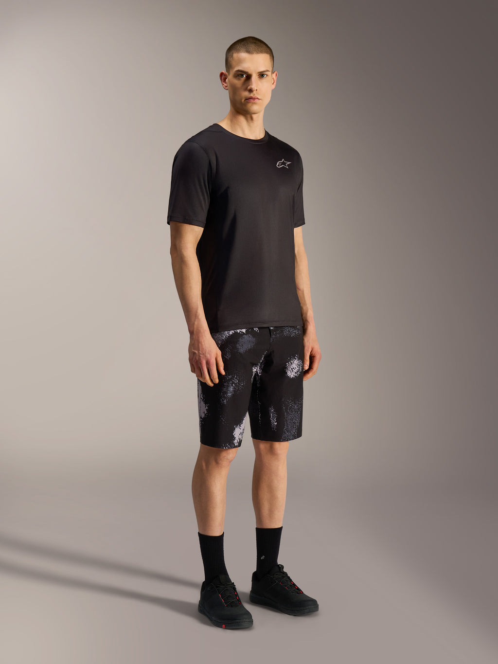 Szorty Alpinestars A-Dura Ride Black Camo, szary wzór kamuflażu, zestawione z czarną koszulką i butami.