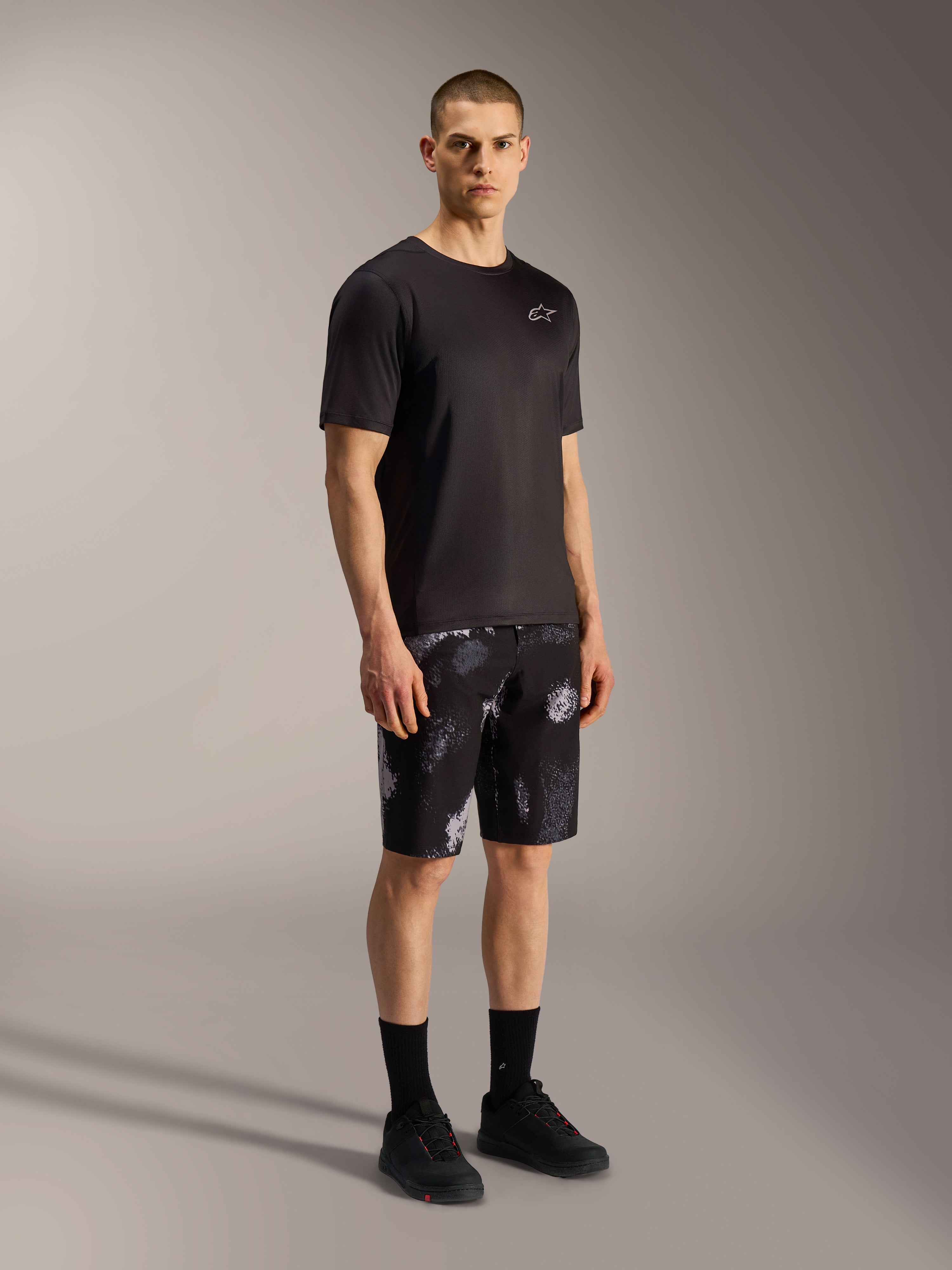 Szorty Alpinestars A-Dura Ride Black Camo, szary wzór kamuflażu, zestawione z czarną koszulką i butami.