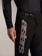 Czarne spodnie MTB Alpinestars A-Supra Elite z zapięciem zapadkowym w pasie i dużym szarym logo Astars na udzie.