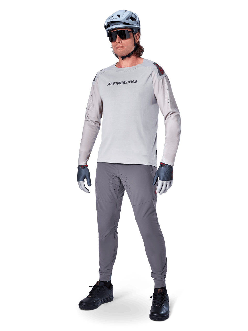 Spodnie Alpinestars A-Aria Elite, ciemnoszare spodnie MTB, noszone przez rowerzystę w jasnoszarej koszulce z długim rękawem i szarym kasku, z laserowo wycinaną wentylacją na udach i dopasowanym sportowym krojem do kolarstwa górskiego.