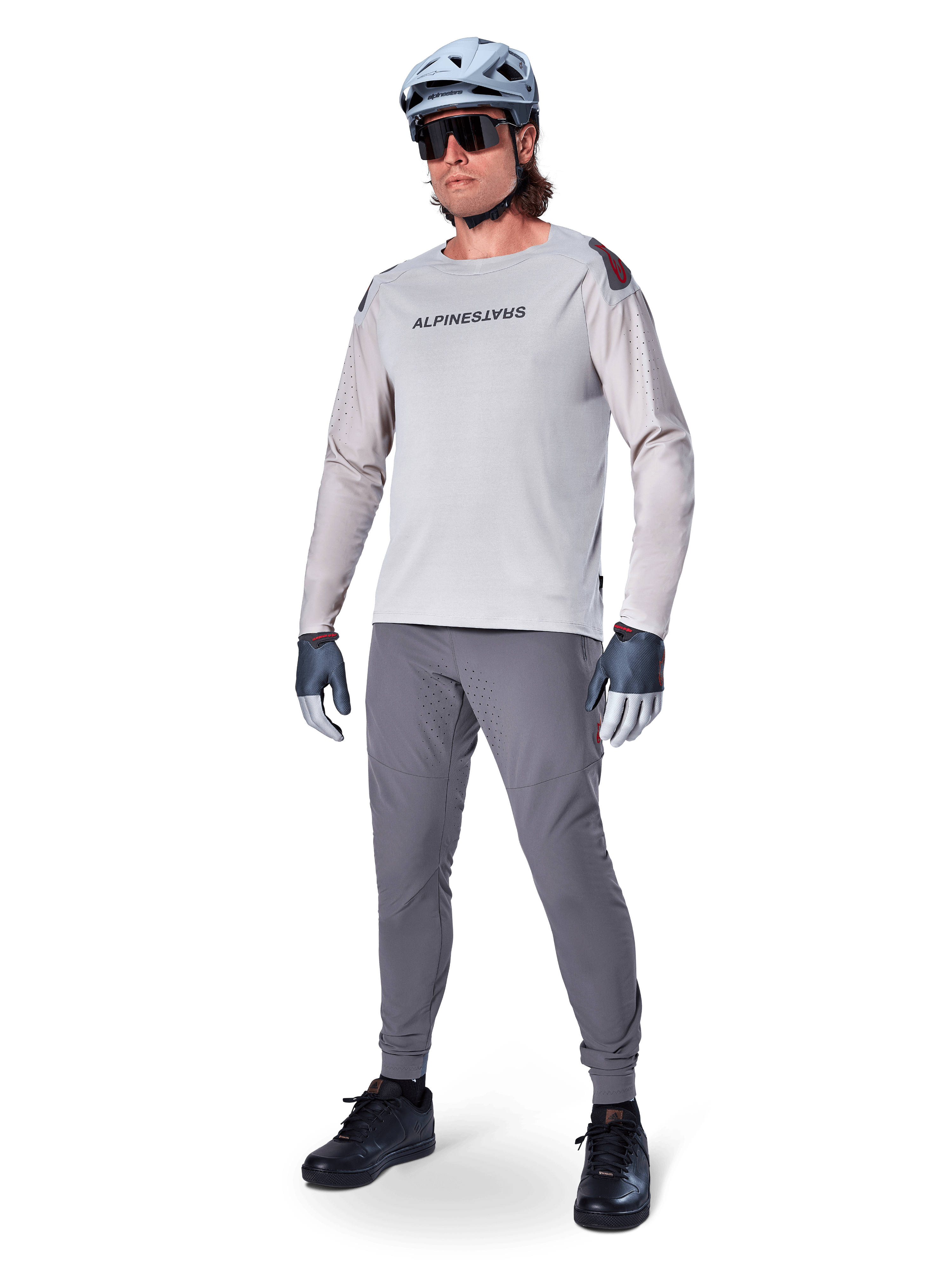 Spodnie Alpinestars A-Aria Elite, ciemnoszare spodnie MTB, noszone przez rowerzystę w jasnoszarej koszulce z długim rękawem i szarym kasku, z laserowo wycinaną wentylacją na udach i dopasowanym sportowym krojem do kolarstwa górskiego.