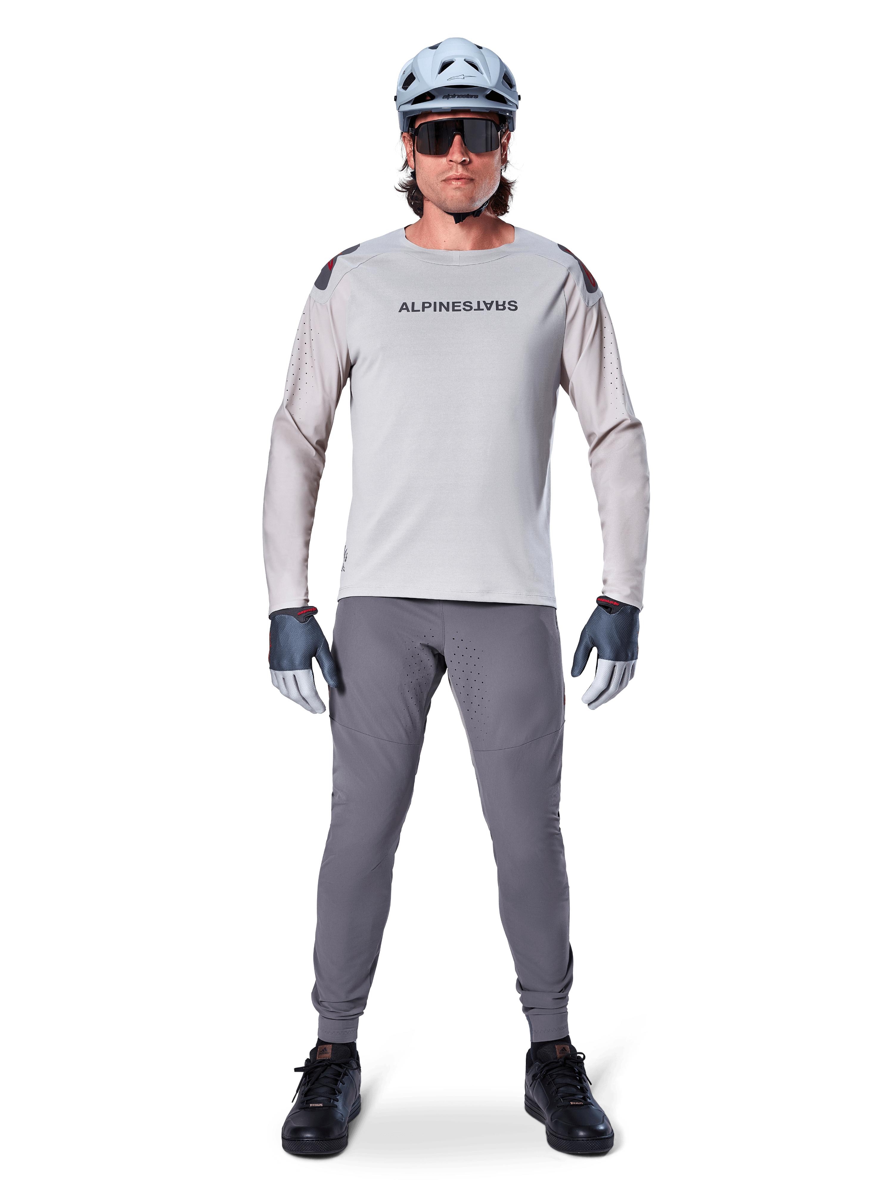 Alpinestars A-Aria Elite Pants, ciemnoszare spodnie rowerowe MTB, noszone przez rowerzystę w jasnoszarej koszulce z długim rękawem, jasnoniebieskim kasku i czarnych butach, z widocznymi laserowymi perforacjami na wewnętrznej stronie nogawek i dopasowanym sportowym krojem.