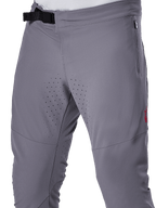 Alpinestars A-Aria Elite Pants, spodnie rowerowe MTB, ciemnoszare, zbliżenie przedstawiające magnetyczne zapięcie na klamrę, boczną kieszeń na zamek oraz laserowo wycinane perforacje wentylacyjne na wewnętrznej stronie ud, zaprojektowane z myślą o wydajności na szlaku.