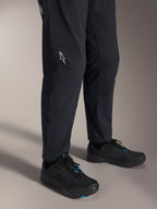 Alpinestars A-Dura Elite Pants, czarne spodnie na rower górski, widok na nogawki z białym logo Alpinestars na kolanie, czarno-niebieskie buty rowerowe, wytrzymała konstrukcja do jazdy MTB