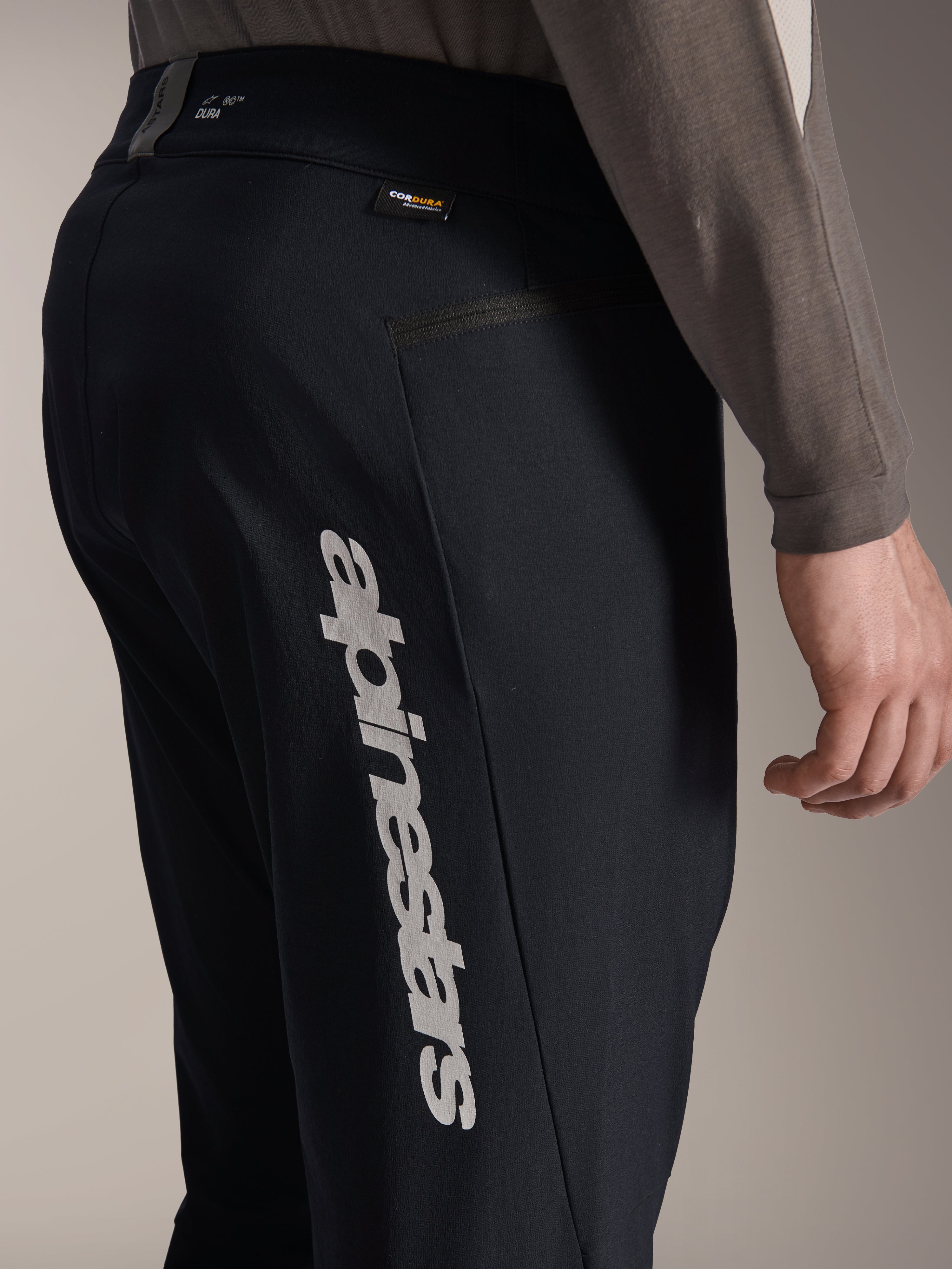 Spodnie Alpinestars A-Dura Elite, czarne spodnie rowerowe MTB, widok z boku z dużym pionowym logo Alpinestars na nogawce, metka tkaniny Cordura i boczna kieszeń na zamek, techniczna odzież rowerowa do jazdy terenowej.