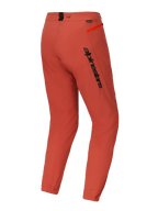 Spodnie Alpinestars A-Dura Elite, spodnie na rower górski (MTB), ciemnopomarańczowe, widok z tyłu pod kątem trzech czwartych, wyraźne czarne logo Alpinestars na udzie, jaskrawopomarańczowy akcent zamka na biodrze, elastyczne ściągacze w kostkach, techniczna odzież rowerowa