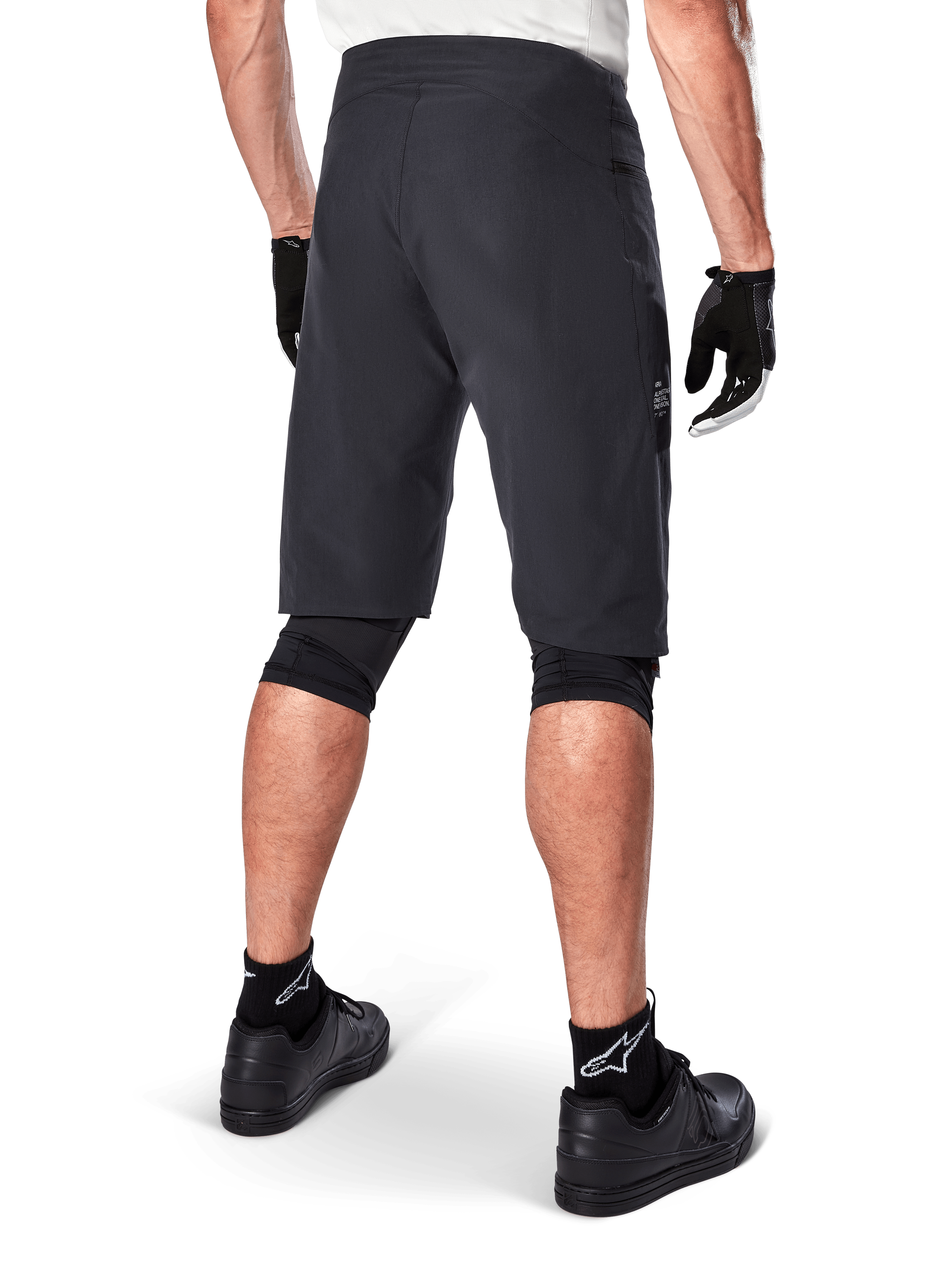 Alpinestars A-Aria Shorts, spodenki rowerowe MTB, czarne, widok z tyłu prezentujący sportowy krój i minimalistyczny design, zestawione z czarnymi rękawiczkami i skarpetami z białym logo Astars, techniczna odzież rowerowa do jazdy w terenie