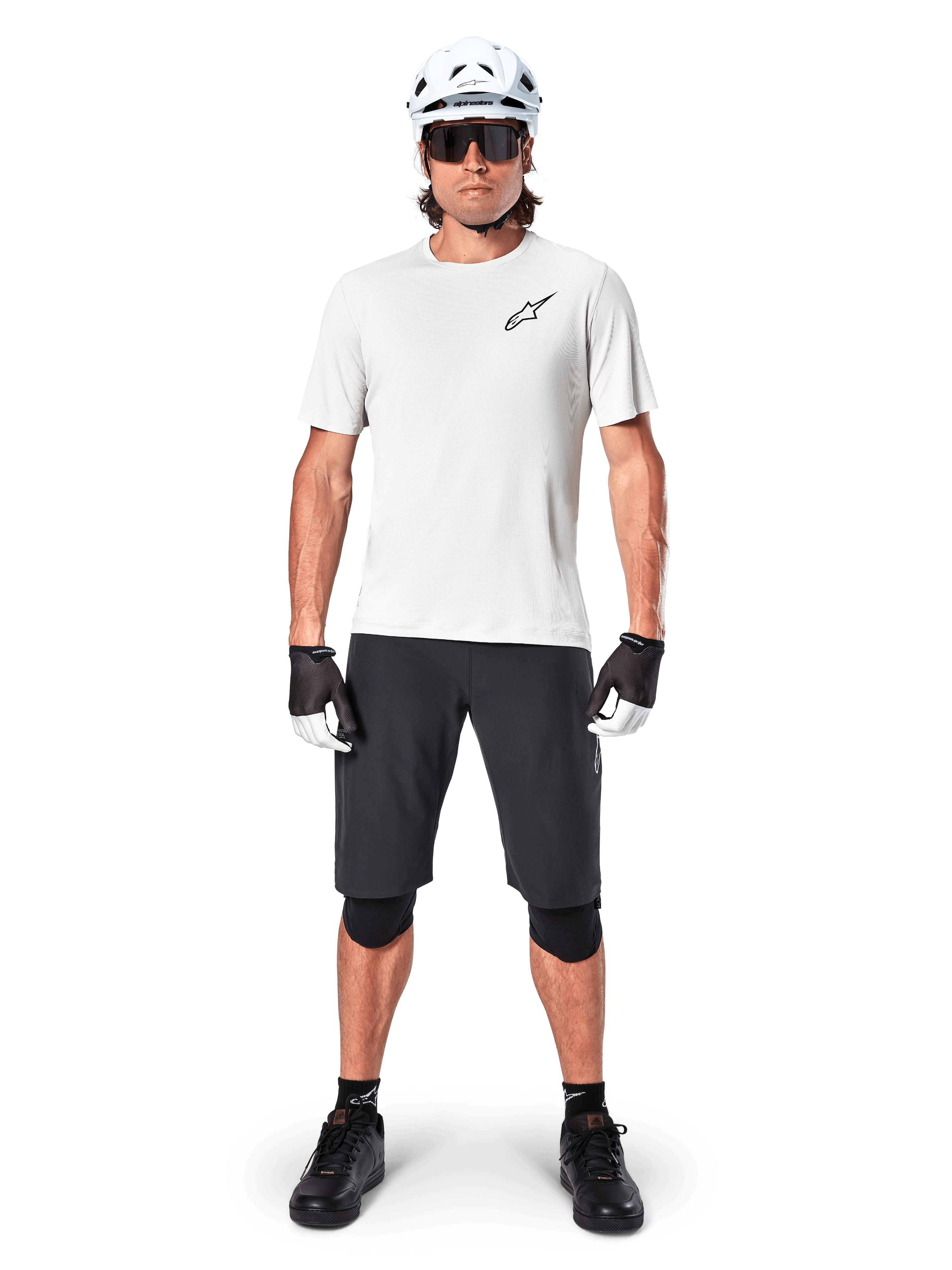 Rowerzysta górski w czarnych spodenkach Alpinestars A-Aria, biała koszulka techniczna, biały kask i czarne ochraniacze na kolana, profesjonalny strój do jazdy terenowej, widok z przodu całej sylwetki