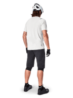 Rowerzysta górski widoczny od tyłu, ubrany w szorty Alpinestars A-Aria w kolorze czarnym, białą techniczną koszulkę z krótkim rękawem, biały kask, czarne rękawiczki i czarne buty MTB, odzież rowerowa do jazdy po szlakach