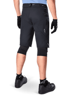 Alpinestars A-Dura Elite Shorts, czarne, widok od tyłu rowerzysty w stroju MTB, w tym czarne nakolanniki, rękawiczki i skarpetki z białym logo, boczne kieszenie na zamek i odblaskowe akcenty, wytrzymały materiał Cordura