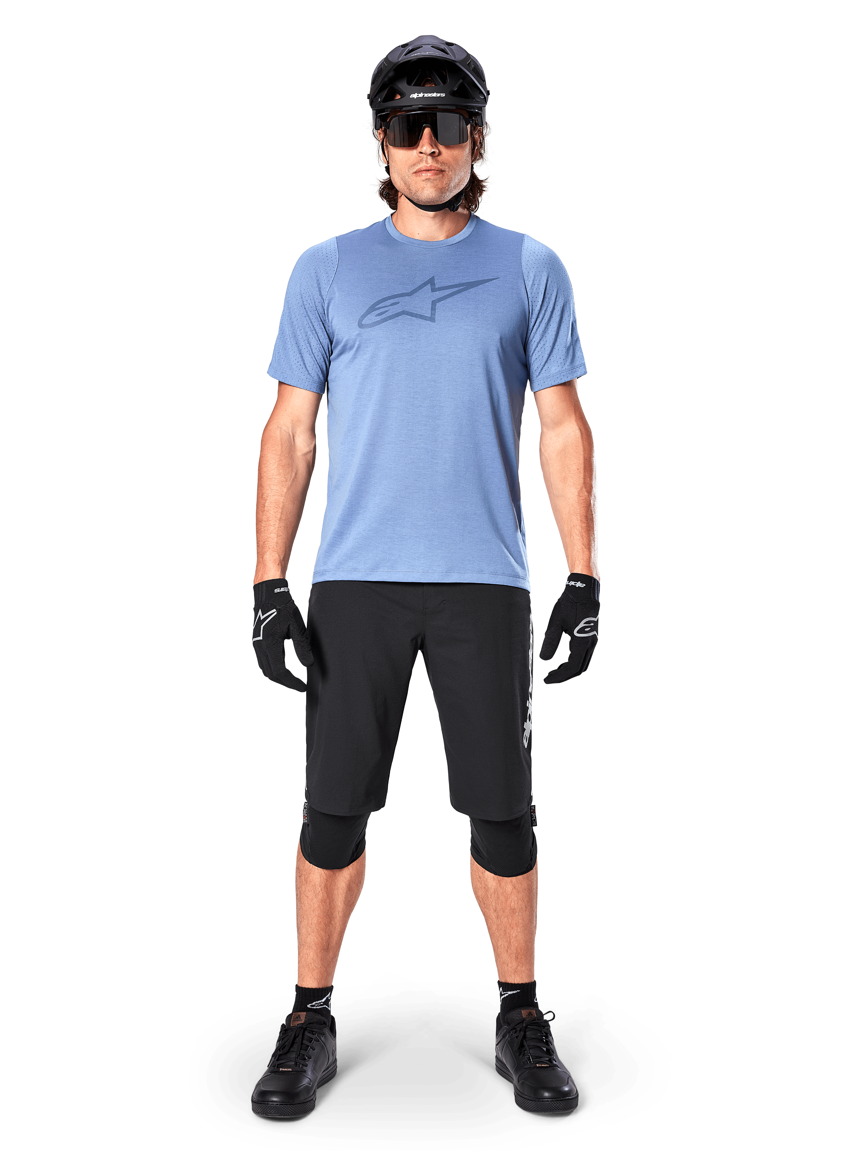Spodenki Alpinestars A-Dura Elite, czarne spodenki MTB, noszone z jasnoniebieską koszulką, czarnym kaskiem, okularami przeciwsłonecznymi i nakolannikami, profesjonalna odzież do kolarstwa terenowego
