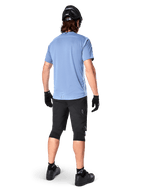 Alpinestars A-Dura Elite Shorts, spodenki rowerowe MTB, czarne, widok z tyłu na modelu, zestaw z jasnoniebieską koszulką z krótkim rękawem i czarnym sprzętem ochronnym, techniczna konstrukcja z kieszeniami na zamek i odblaskowymi detalami do jazdy w terenie