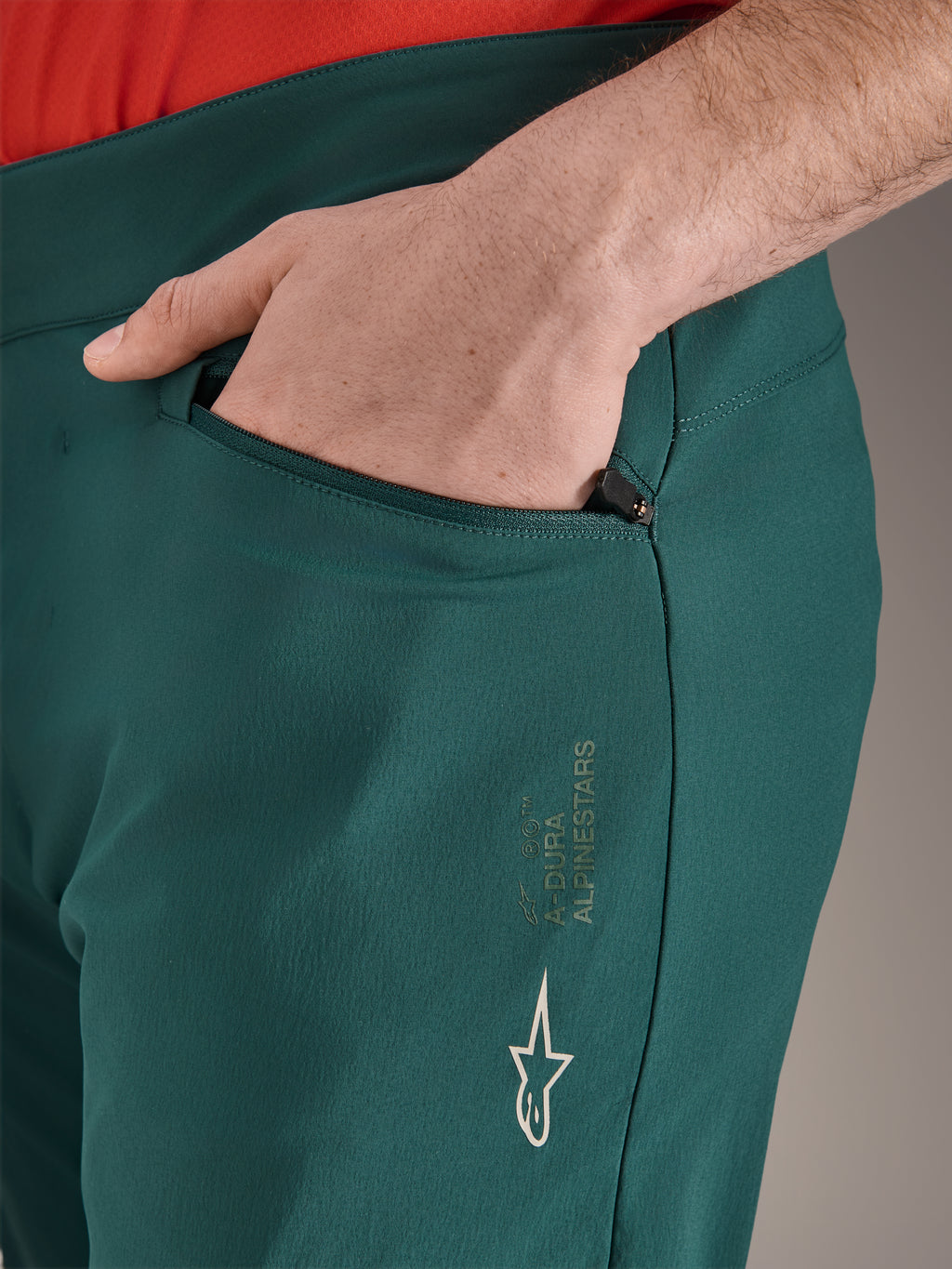 Spodnie Alpinestars A-Dura w kolorze Dark Pine, zbliżenie na kieszeń zapinaną na zamek z dłonią, białe logo i branding Alpinestars na udzie, wytrzymałe spodnie rowerowe MTB