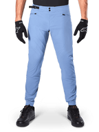 Alpinestars A-Dura Pants, spodnie MTB, Infinity Blue, jasnoniebieskie spodnie rowerowe górskie z podwójnym zapięciem na zatrzaski i kieszeniami na zamek, noszone z czarnymi rękawiczkami i czarnymi butami, regularny krój z elastycznymi mankietami