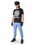 Spodnie Alpinestars A-Dura, spodnie MTB, Infinity Blue, noszone z czarnym t-shirtem z białym spiralnym logo, czarnym kaskiem, okularami przeciwsłonecznymi i czarnymi rękawiczkami, profesjonalny sprzęt do kolarstwa górskiego
