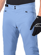 Alpinestars A-Dura Pants, spodnie rowerowe MTB, kolor Infinity Blue, zbliżenie na talię z podwójnym zapięciem na zatrzaski i bocznym regulatorem, kieszenie na zamek, noszone z czarnymi rękawicami Alpinestars