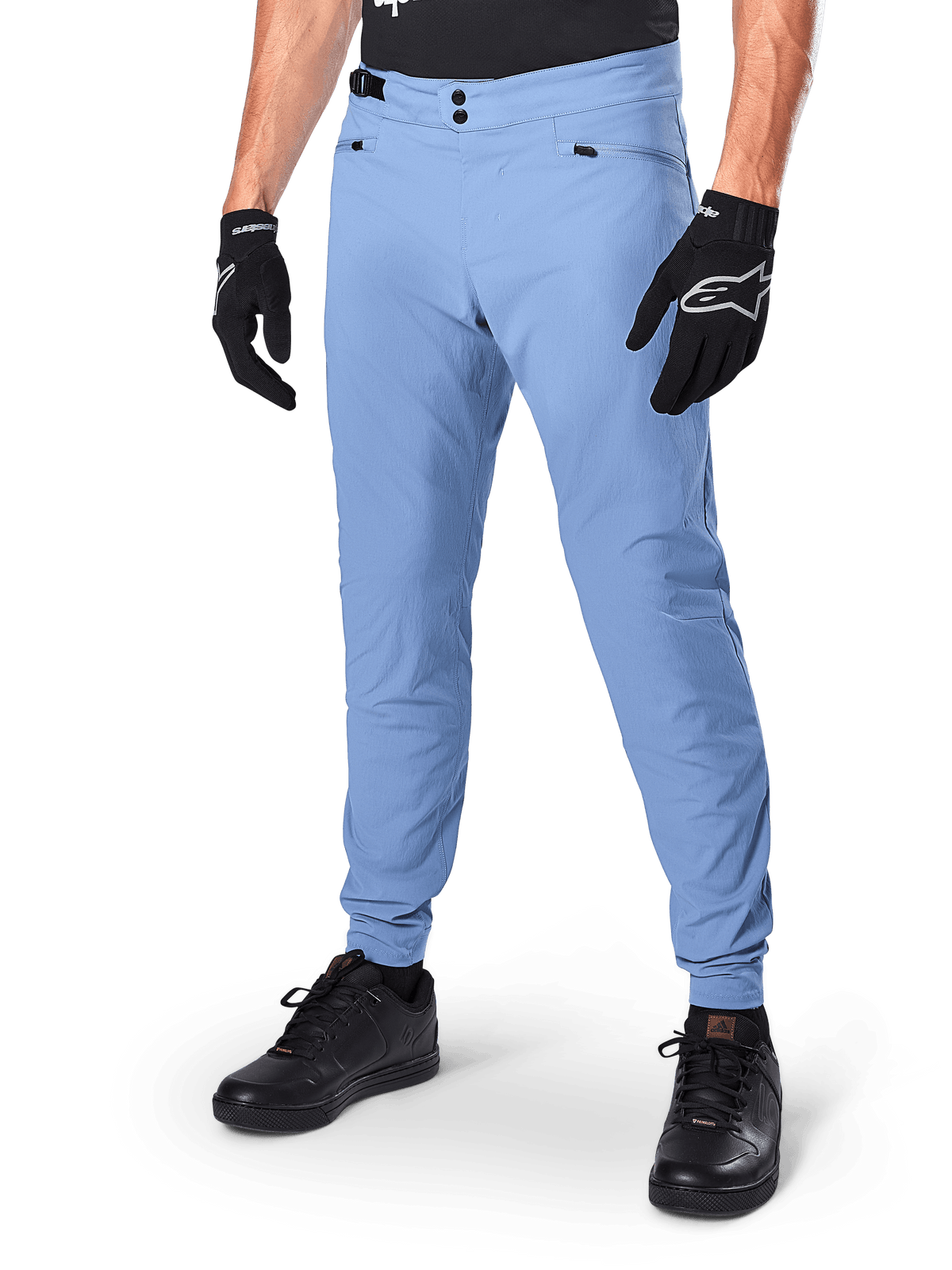Alpinestars A-Dura Pants, spodnie rowerowe MTB w kolorze Infinity Blue, z podwójnym zapięciem na zatrzaski i kieszeniami na zamek, noszone z czarnymi rękawiczkami i czarnymi butami, wytrzymały materiał rozciągliwy w dwóch kierunkach do jazdy w terenie