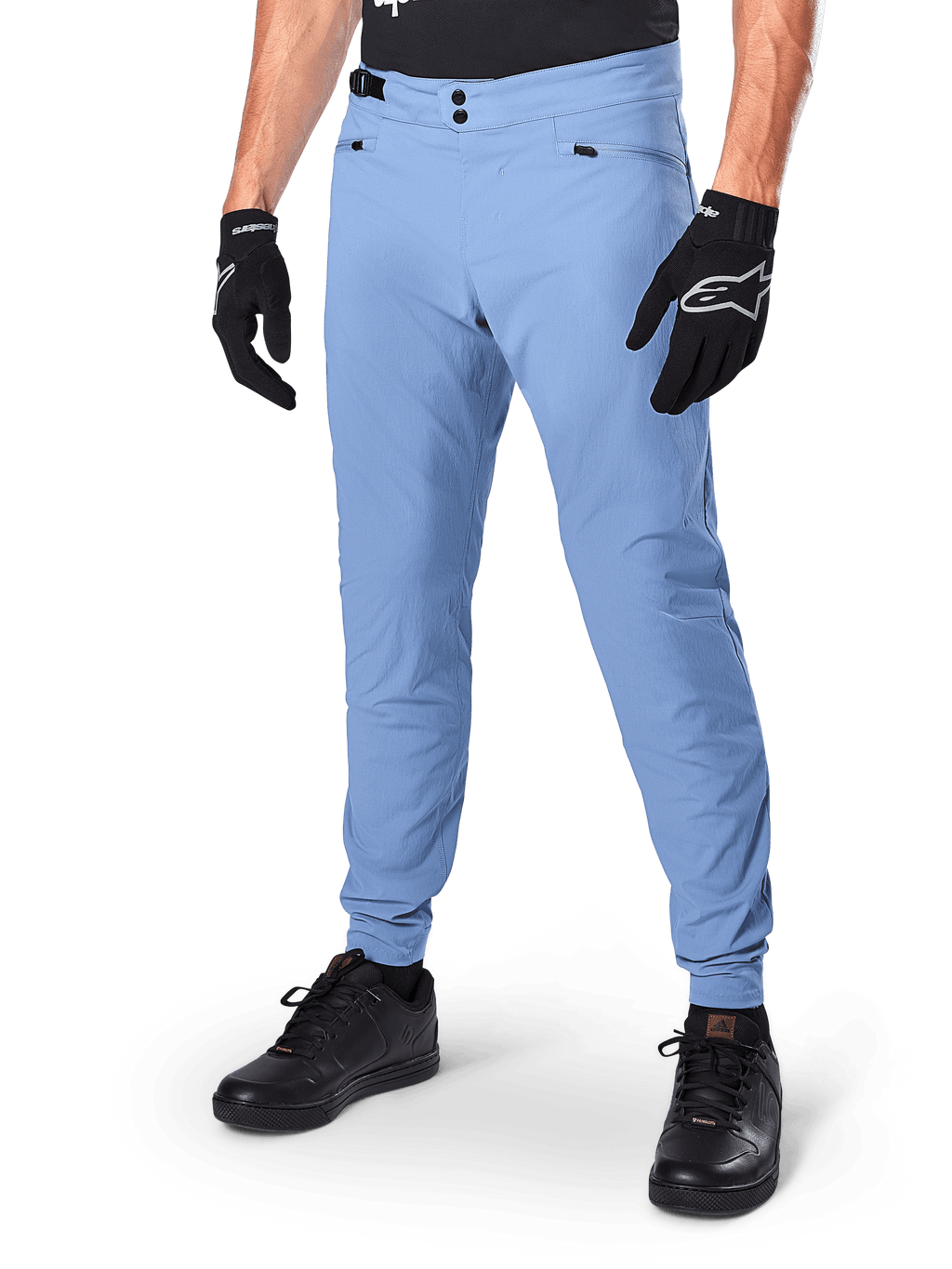 Alpinestars A-Dura Pants, spodnie rowerowe MTB w kolorze Infinity Blue, z podwójnym zapięciem na zatrzaski i kieszeniami na zamek, noszone z czarnymi rękawiczkami i czarnymi butami, wytrzymały materiał rozciągliwy w dwóch kierunkach do jazdy w terenie