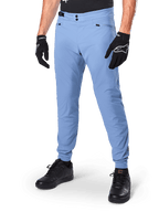 Alpinestars A-Dura Pants, spodnie rowerowe MTB w kolorze Infinity Blue, z podwójnym zapięciem na zatrzaski i kieszeniami na zamek, noszone z czarnymi rękawiczkami i czarnymi butami, wytrzymały materiał rozciągliwy w dwóch kierunkach do jazdy w terenie