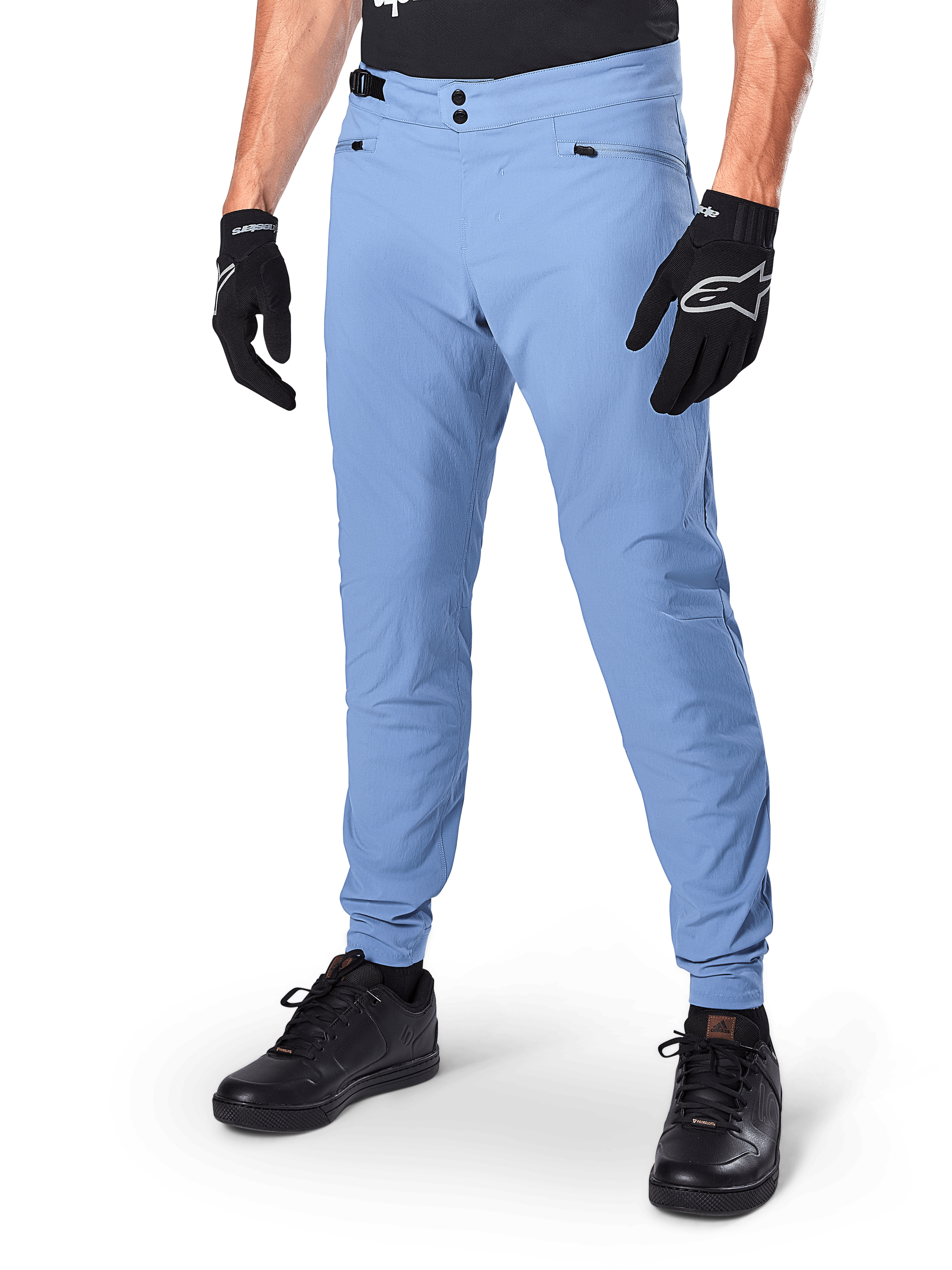 Alpinestars A-Dura Pants, spodnie rowerowe MTB w kolorze Infinity Blue, z podwójnym zapięciem na zatrzaski i kieszeniami na zamek, noszone z czarnymi rękawiczkami i czarnymi butami, wytrzymały materiał rozciągliwy w dwóch kierunkach do jazdy w terenie