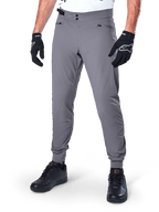 Alpinestars A-Dura Pants, ciemnoszare spodnie MTB, z podwójnym zapięciem na zatrzaski w pasie i kieszeniami na suwak, elastyczne mankiety, noszone z czarnymi rękawicami rowerowymi i czarnymi sneakersami