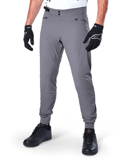 Alpinestars A-Dura Pants, Dark Gray MTB Pants, featuring double snap waist closure and zippered pockets, elasticated cuffs, worn with black cycling gloves and black sneakers