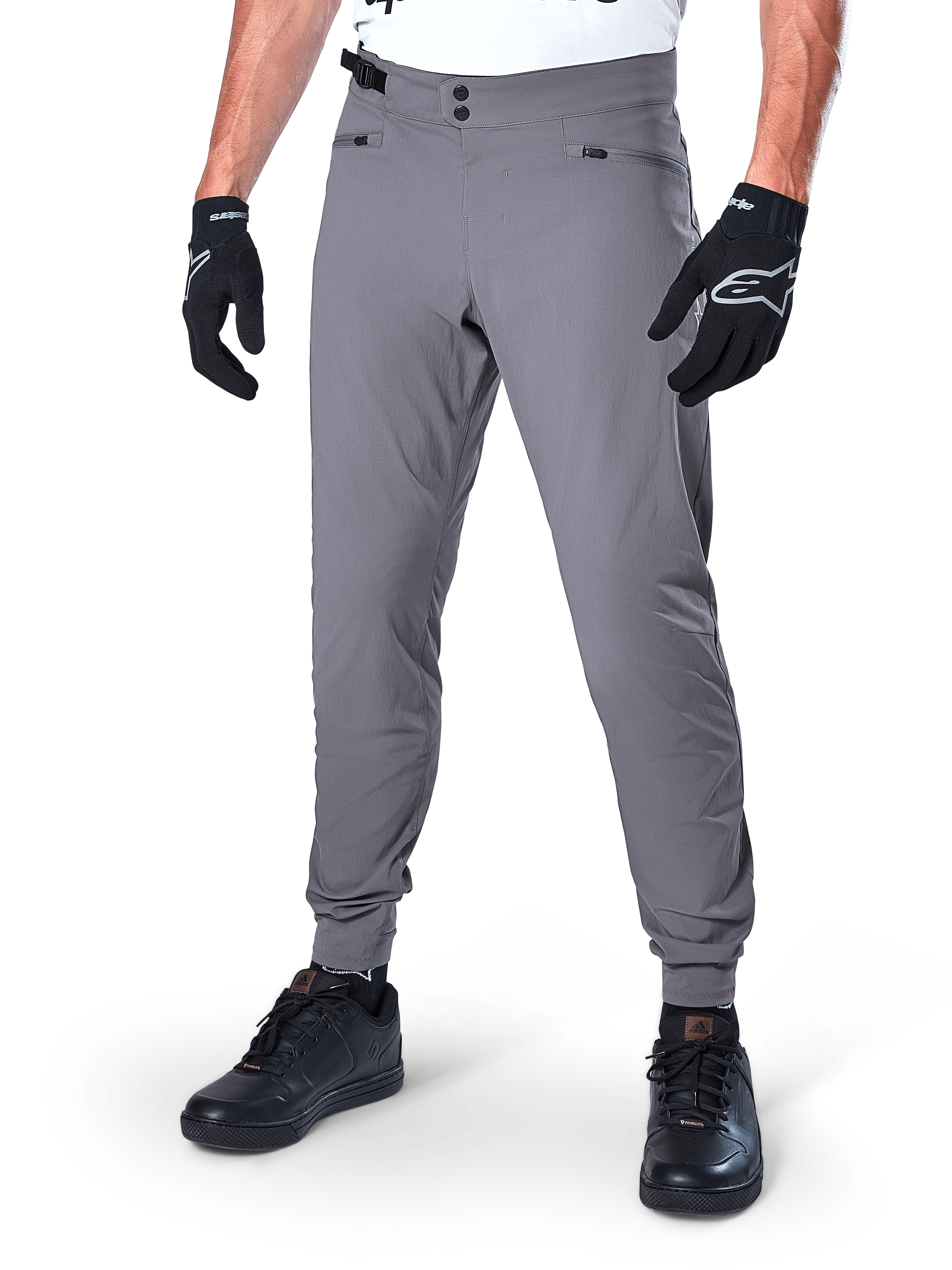 Alpinestars A-Dura Pants, ciemnoszare spodnie MTB, z podwójnym zapięciem na zatrzaski w pasie i kieszeniami na suwak, elastyczne mankiety, noszone z czarnymi rękawicami rowerowymi i czarnymi sneakersami