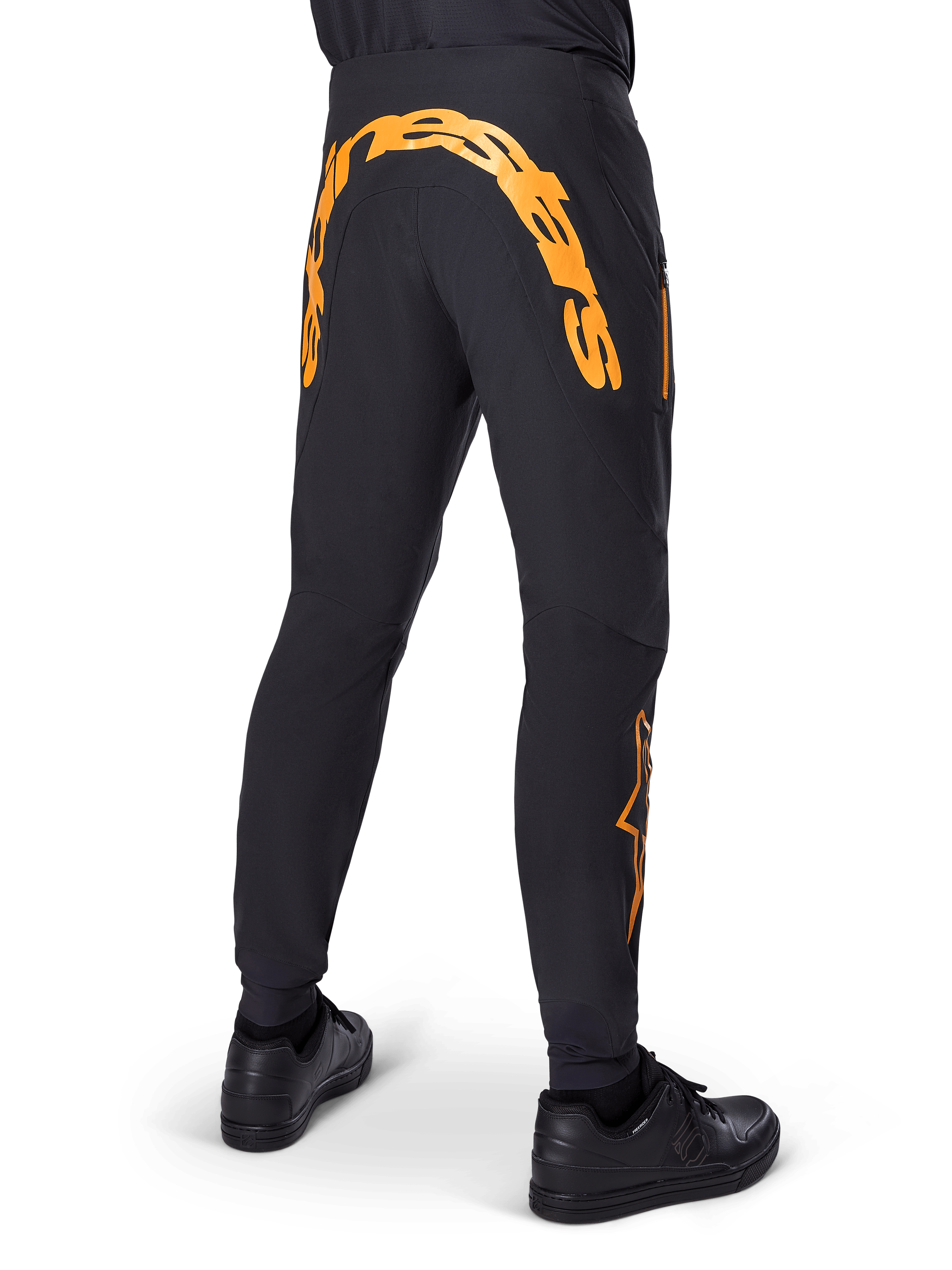 Alpinestars A-Supra Race Pants, czarne spodnie MTB, widok z tyłu z dużym pomarańczowym napisem Alpinestars na karczku, pomarańczowe logo na dolnej części nogawki, sportowy krój z kieszenią na zamek, czarne buty