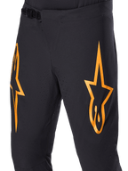 Alpinestars A-Supra Race Pants, czarne spodnie rowerowe MTB z dużymi pomarańczowymi logotypami gwiazdy, wyposażone w przednie zapięcie na zapadkę i laserowo wycinane otwory wentylacyjne, techniczny design zorientowany na wydajność.