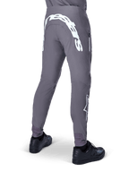 Alpinestars A-Supra Race Pants, spodnie rowerowe MTB, ciemnoszare, widok z tyłu, czarne buty, duży biały napis Alpinestars na karczku i logo gwiazdy na nogawce, kieszeń zapinana na zamek, elastyczny materiał techniczny do wyścigów MTB