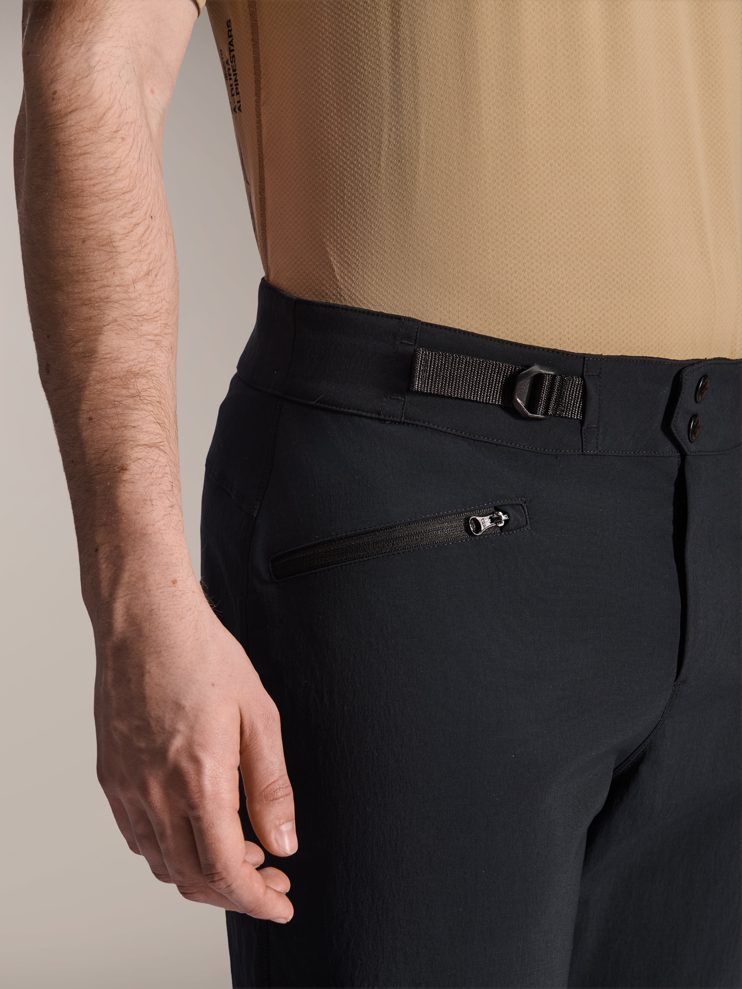 Alpinestars A-Dura Shorts, czarne spodenki MTB, zbliżenie na kieszeń zapinaną na zamek i regulowany boczny ściągacz, podwójne zapięcie na napy, wytrzymały materiał do kolarstwa górskiego
