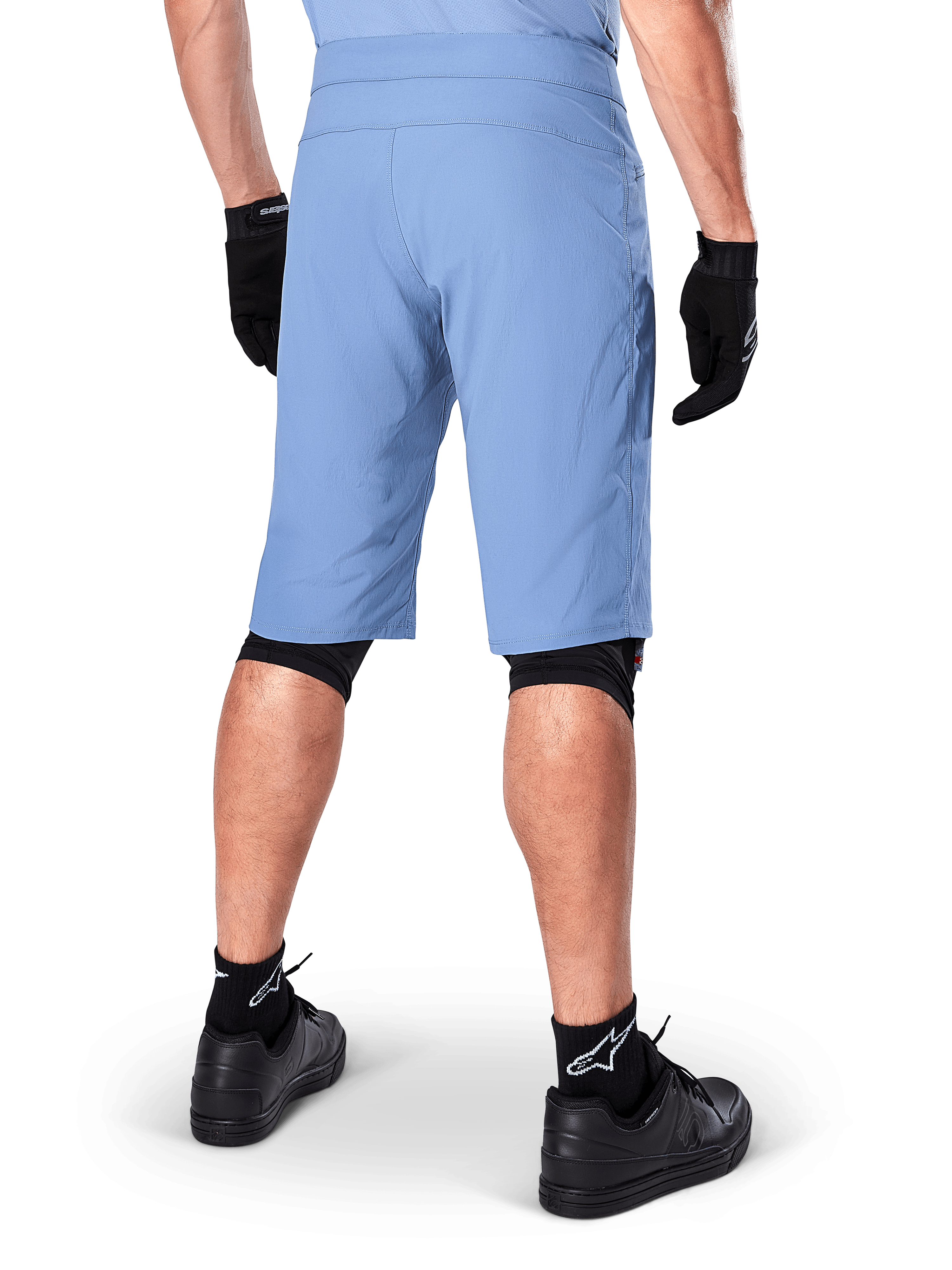 Alpinestars A-Dura Shorts, spodenki MTB w kolorze Infinity Blue, widok z tyłu, zestawione z czarnymi rękawiczkami, nakolannikami i czarnymi skarpetkami z białym logo gwiazdy, wytrzymały, rozciągliwy materiał do jazdy w terenie