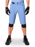 Alpinestars A-Dura Shorts, spodenki do kolarstwa górskiego w kolorze Infinity Blue, noszone z czarnymi rękawiczkami i nakolannikami, wyposażone w podwójne zapięcie na napy i boczną regulację w talii, wyczynowa odzież rowerowa do MTB