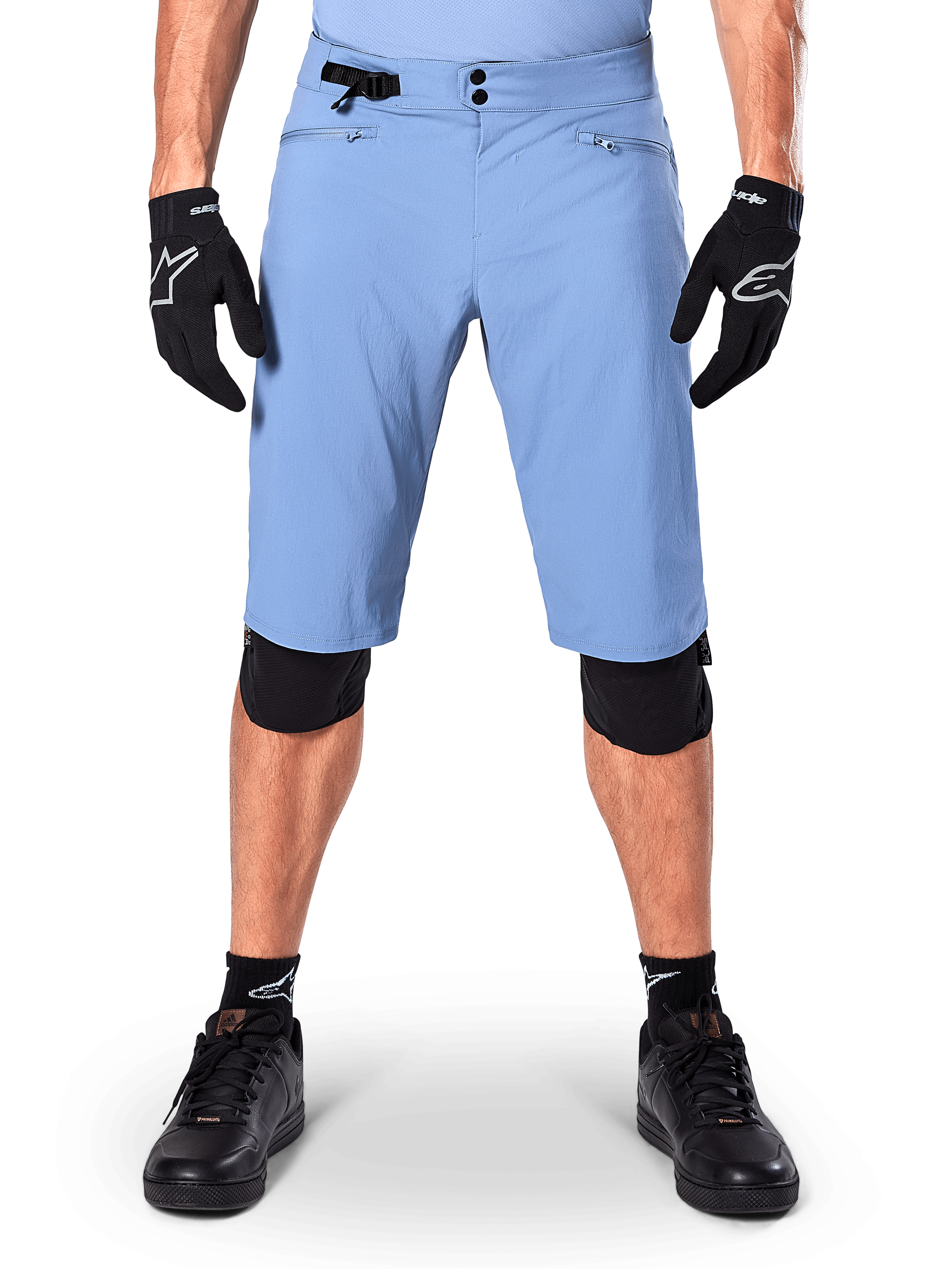 Alpinestars A-Dura Shorts, spodenki do kolarstwa górskiego w kolorze Infinity Blue, noszone z czarnymi rękawiczkami i nakolannikami, wyposażone w podwójne zapięcie na napy i boczną regulację w talii, wyczynowa odzież rowerowa do MTB