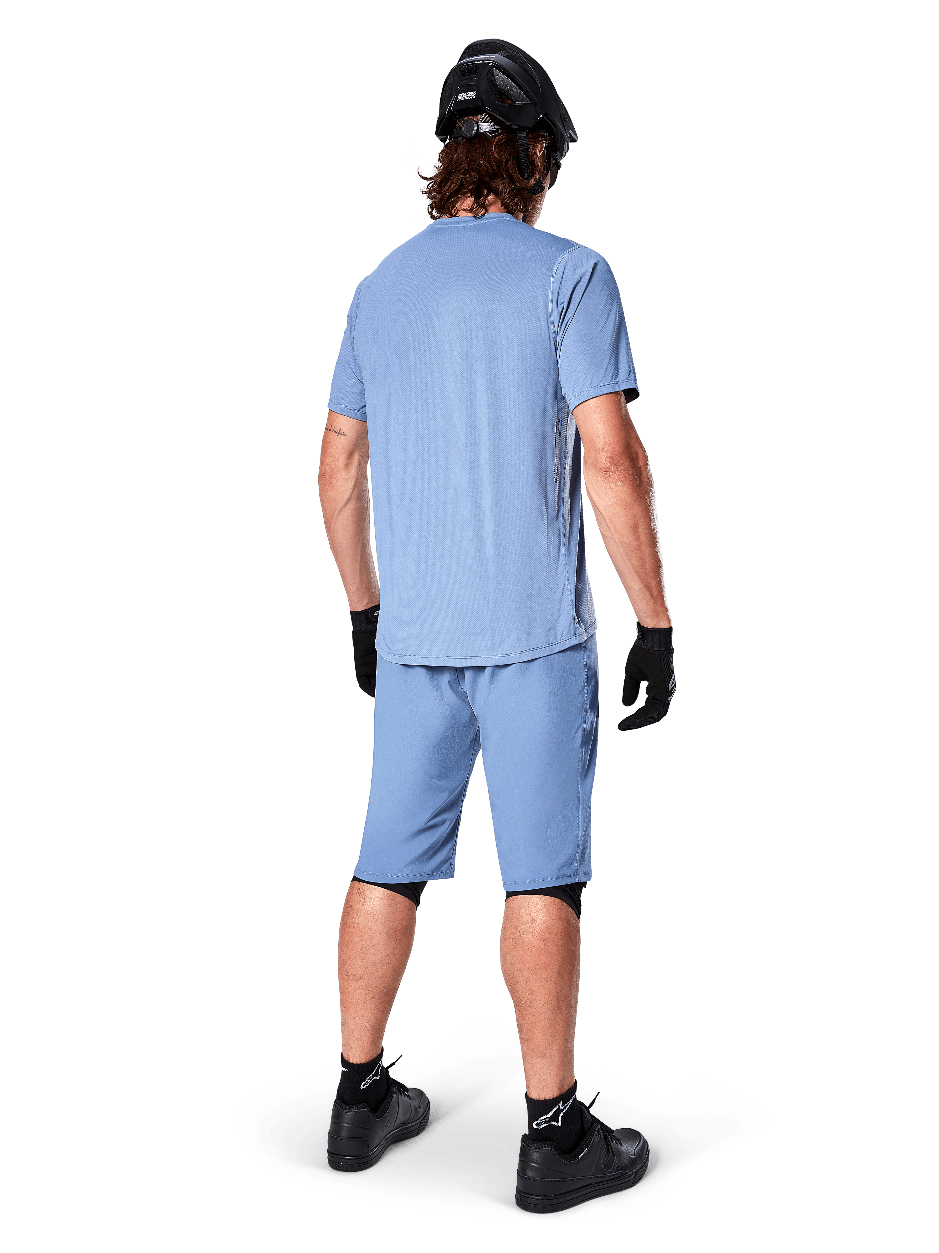 Widok z tyłu rowerzysty górskiego ubranego w spodenki Alpinestars A-Dura w kolorze Infinity Blue, pasującą koszulkę z krótkim rękawem, czarny kask, czarne rękawiczki i czarne buty, skoordynowana odzież wyczynowa do jazdy na szlakach MTB