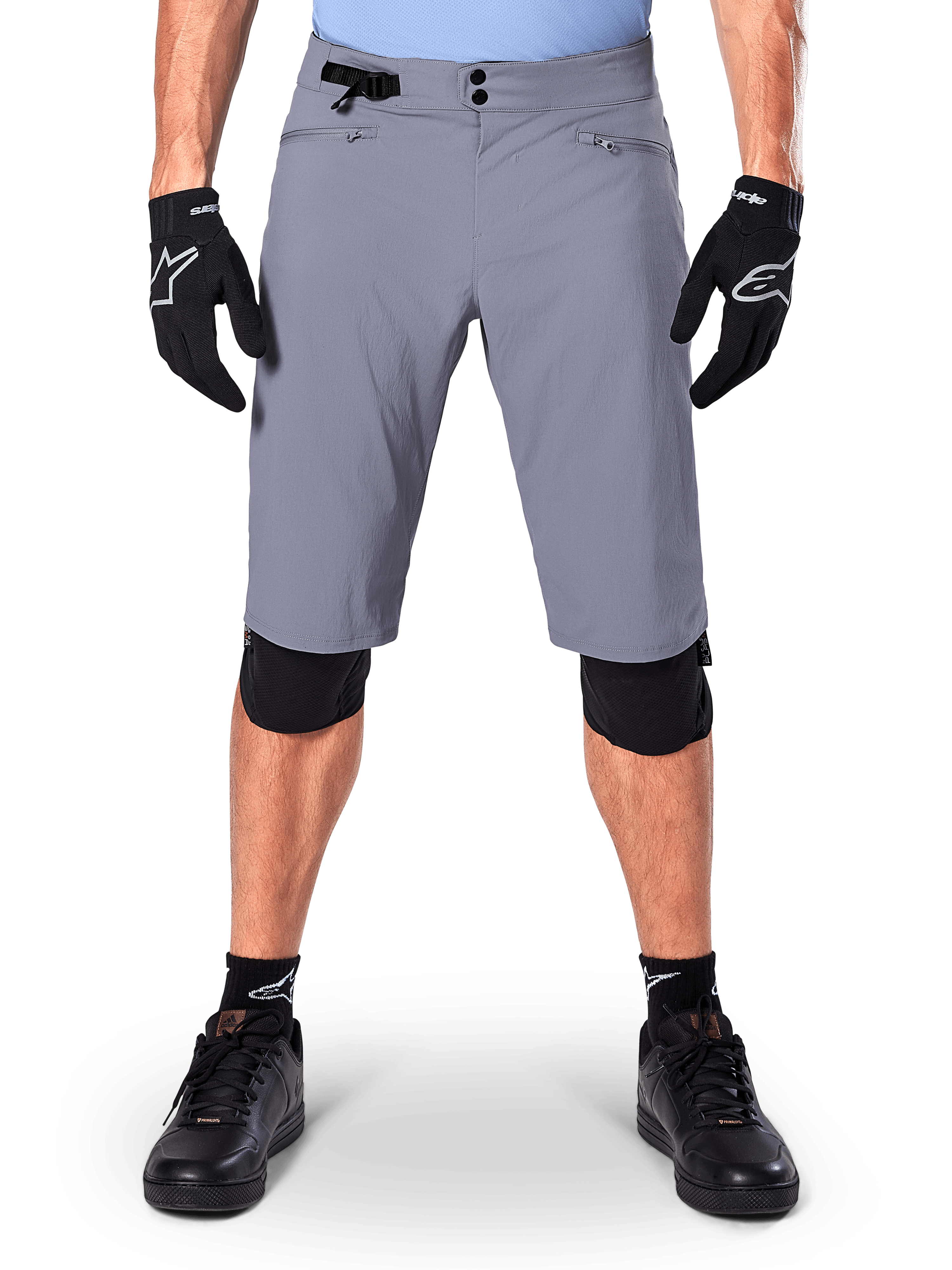 Alpinestars A-Dura Shorts, spodenki MTB, ciemnoszare, noszone z czarnymi rękawiczkami i ochraniaczami kolan Alpinestars, z podwójnym zapięciem na napy i kieszeniami na zamek z podszewką z siatki, wytrzymały materiał rozciągliwy w dwóch kierunkach do kolarstwa górskiego