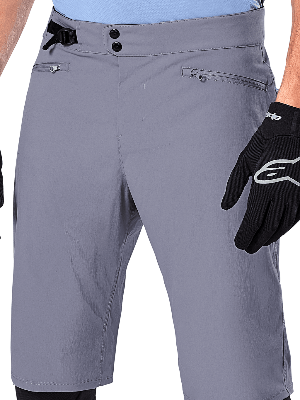 Alpinestars A-Dura Shorts, spodenki MTB, ciemnoszare, zbliżenie na talię pokazujące podwójne zapięcie na napy, boczny ściągacz i kieszenie zapinane na zamek, czarne rękawiczki rowerowe, wytrzymała odzież do kolarstwa górskiego.
