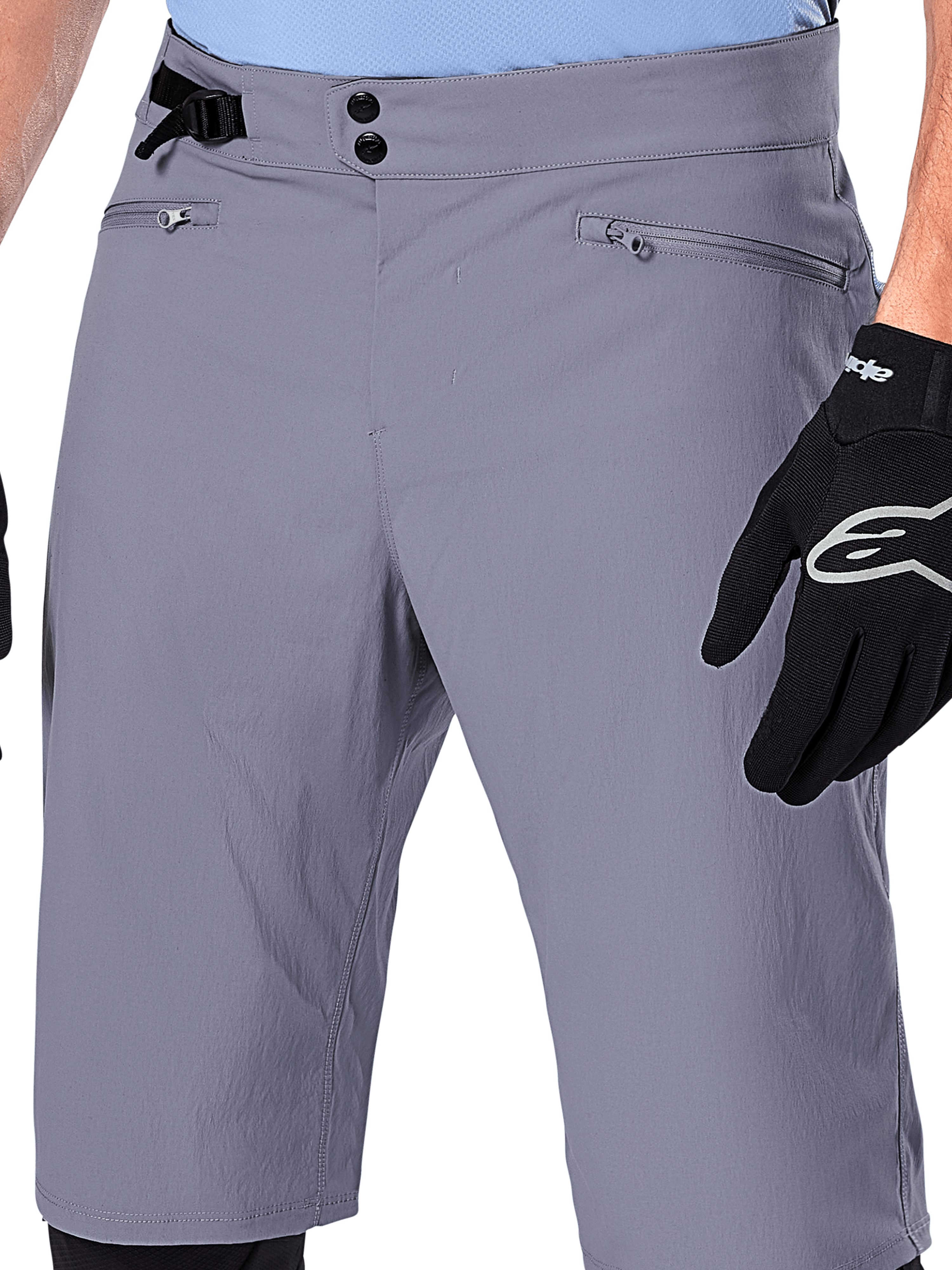 Alpinestars A-Dura Shorts, spodenki MTB, ciemnoszare, zbliżenie na talię pokazujące podwójne zapięcie na napy, boczny ściągacz i kieszenie zapinane na zamek, czarne rękawiczki rowerowe, wytrzymała odzież do kolarstwa górskiego.