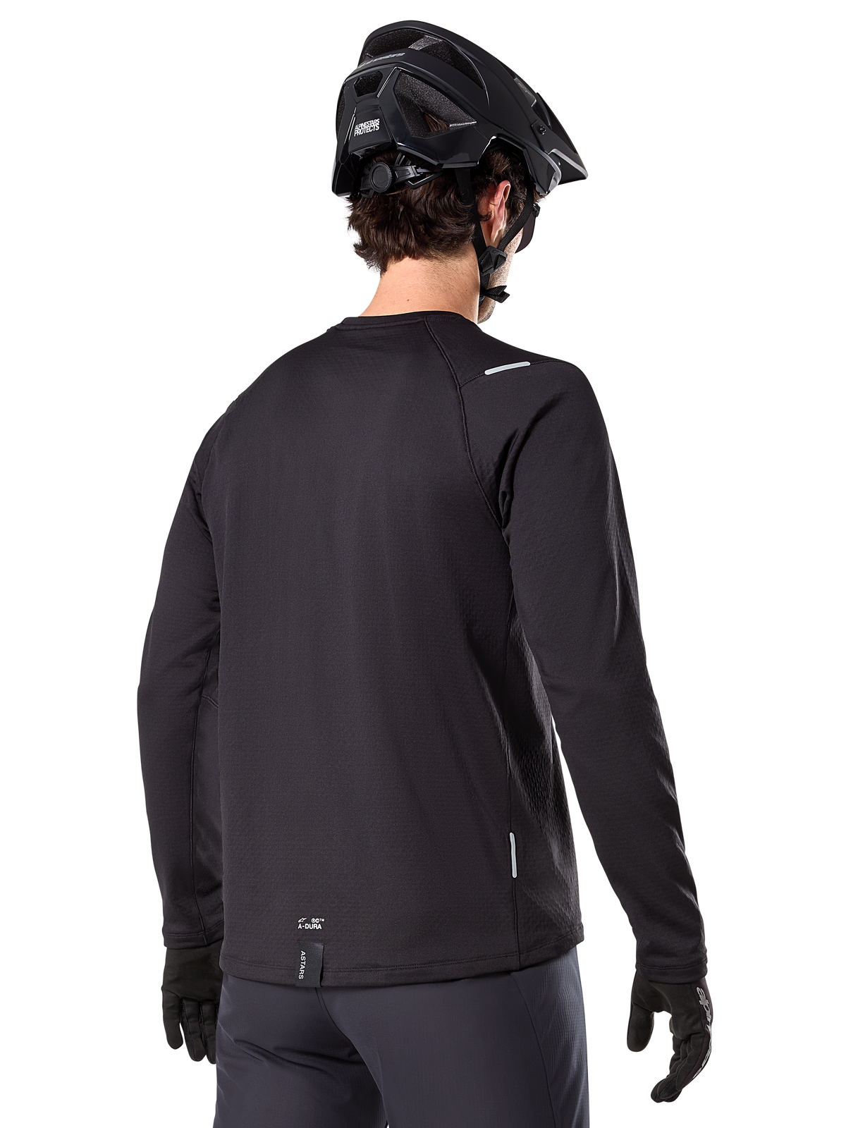 Alpinestars A-Dura Thermal Jersey, koszulka rowerowa MTB z długim rękawem, czarna, widok z tyłu pokazujący przedłużony tył, małe odblaskowe detale i logo na dolnej krawędzi, noszona z czarnym kaskiem i rękawiczkami do jazdy w chłodne dni