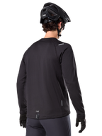 Alpinestars A-Dura Thermal Jersey, koszulka rowerowa MTB z długim rękawem, czarna, widok z tyłu pokazujący przedłużony tył, małe odblaskowe detale i logo na dolnej krawędzi, noszona z czarnym kaskiem i rękawiczkami do jazdy w chłodne dni