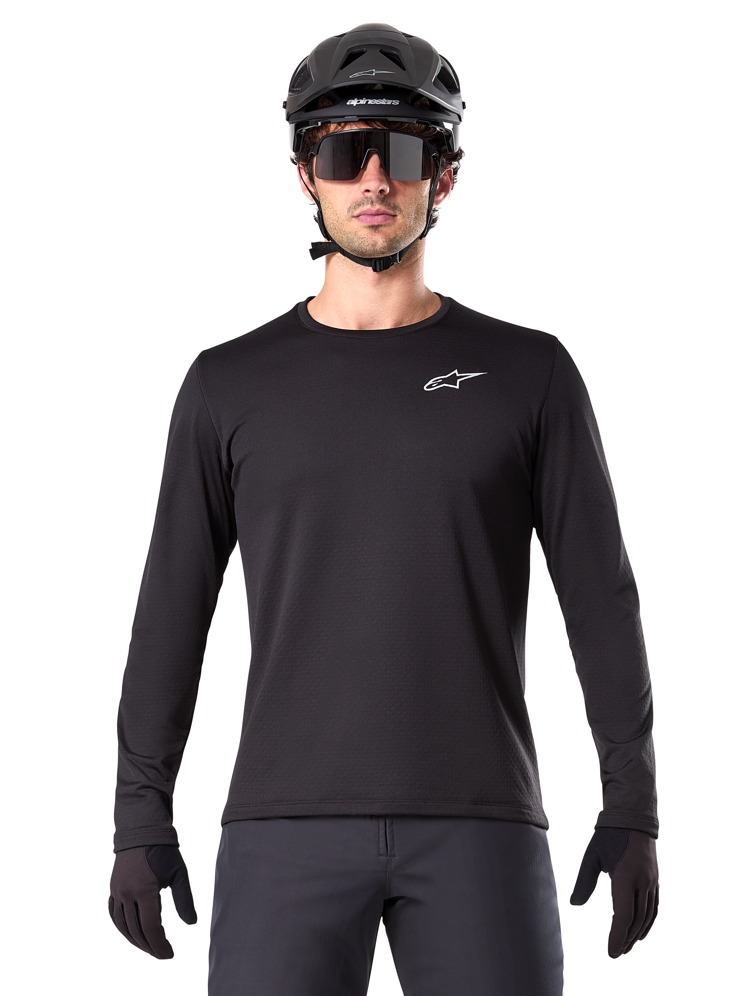 Alpinestars A-Dura Thermal Jersey, czarna koszulka rowerowa MTB z długim rękawem, noszona z czarnym kaskiem i dużymi okularami przeciwsłonecznymi, małe białe logo Alpinestars na piersi, regularny krój, odzież rowerowa MTB