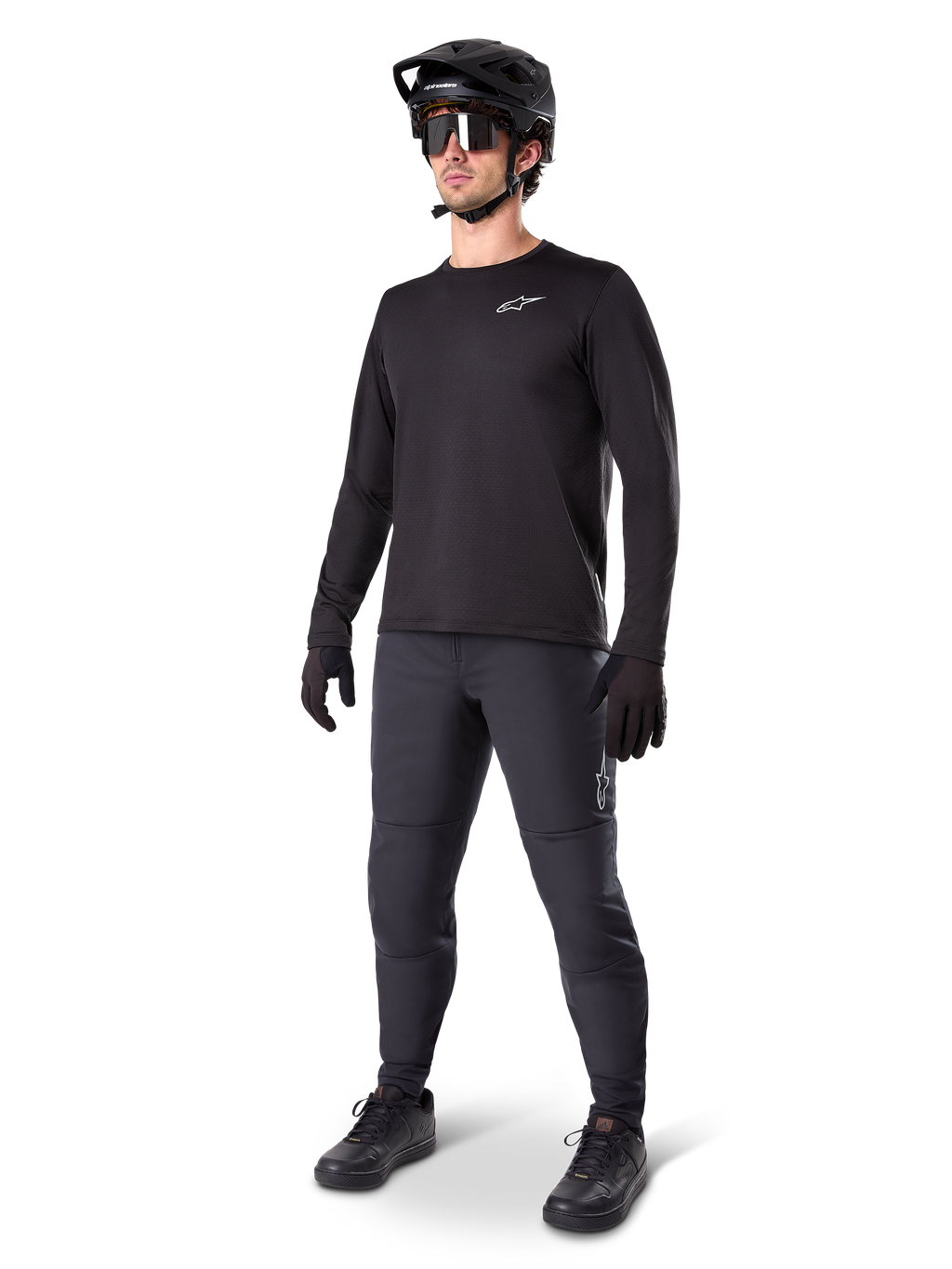 Model w koszulce termicznej Alpinestars A-Dura, czarna koszulka MTB z długim rękawem, czarny kask rowerowy MTB, okulary przeciwsłoneczne i ciemnoszare spodnie, małe białe logo na piersi, izolująca konstrukcja polarowa do jazdy w chłodne dni