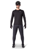 Alpinestars A-Dura Thermal Jersey, czarna koszulka rowerowa z długim rękawem, noszona z ciemnoszarymi spodniami, czarnymi rękawiczkami, czarnym kaskiem i okularami przeciwsłonecznymi, białe logo Alpinestars na piersi, dopasowany strój do jazdy na rowerze górskim w chłodne dni