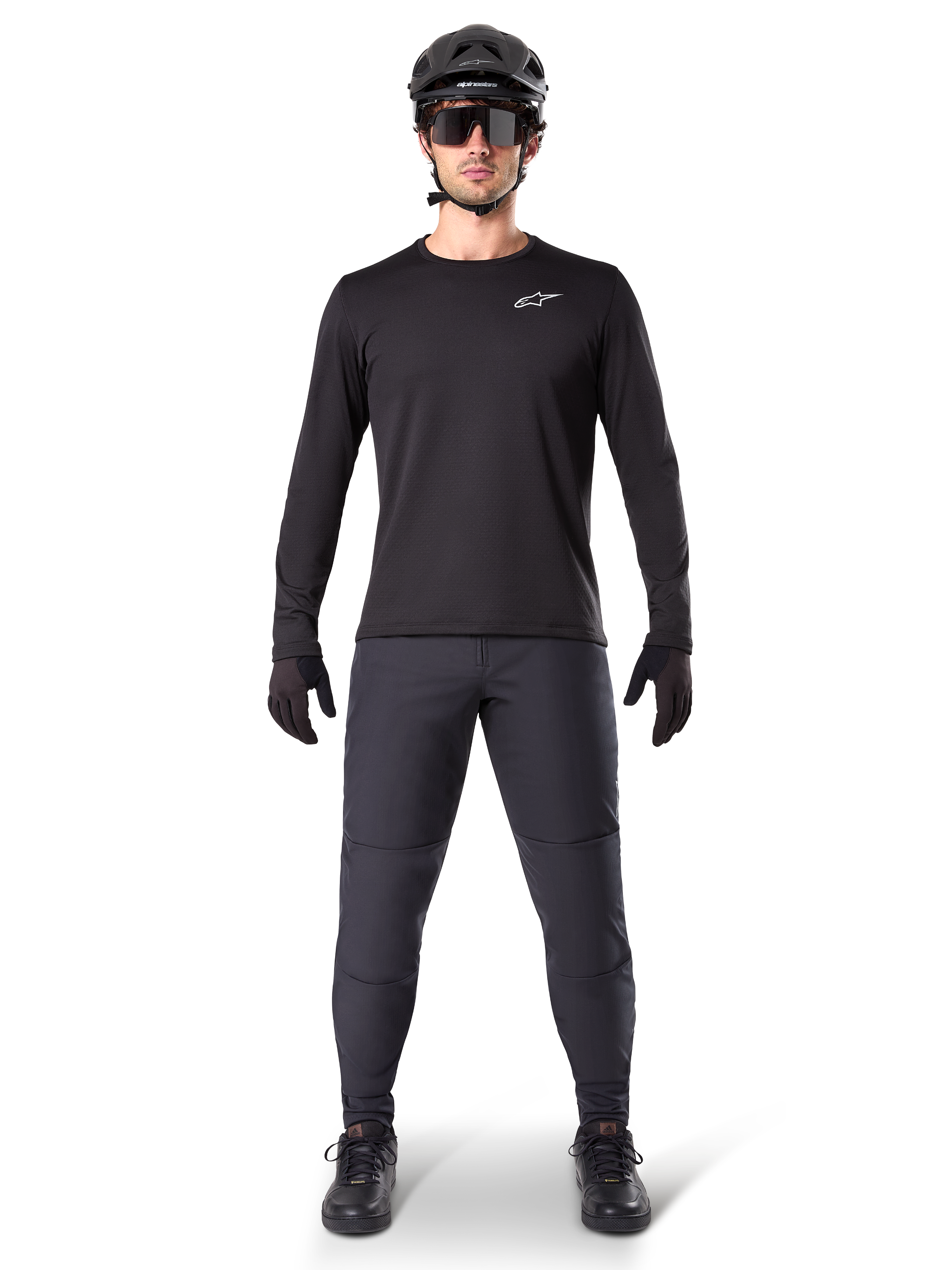 Alpinestars A-Dura Thermal Jersey, czarna koszulka rowerowa z długim rękawem, noszona z ciemnoszarymi spodniami, czarnymi rękawiczkami, czarnym kaskiem i okularami przeciwsłonecznymi, białe logo Alpinestars na piersi, dopasowany strój do jazdy na rowerze górskim w chłodne dni