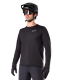 Alpinestars A-Dura Thermal Jersey, czarna koszulka MTB z długim rękawem, białe logo na piersi, noszona z czarnym kaskiem i rękawicami, nowoczesny sportowy design do jazdy na szlaku