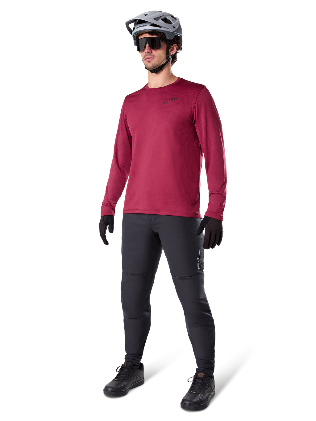 Alpinestars A-Dura Thermal Jersey w kolorze bordowym, ocieplana koszulka rowerowa z długim rękawem noszona z ciemnoszarymi spodniami MTB, czarnymi rękawiczkami i szarym kaskiem, ujęcie studyjne całej sylwetki odzieży rowerowej na zimne dni