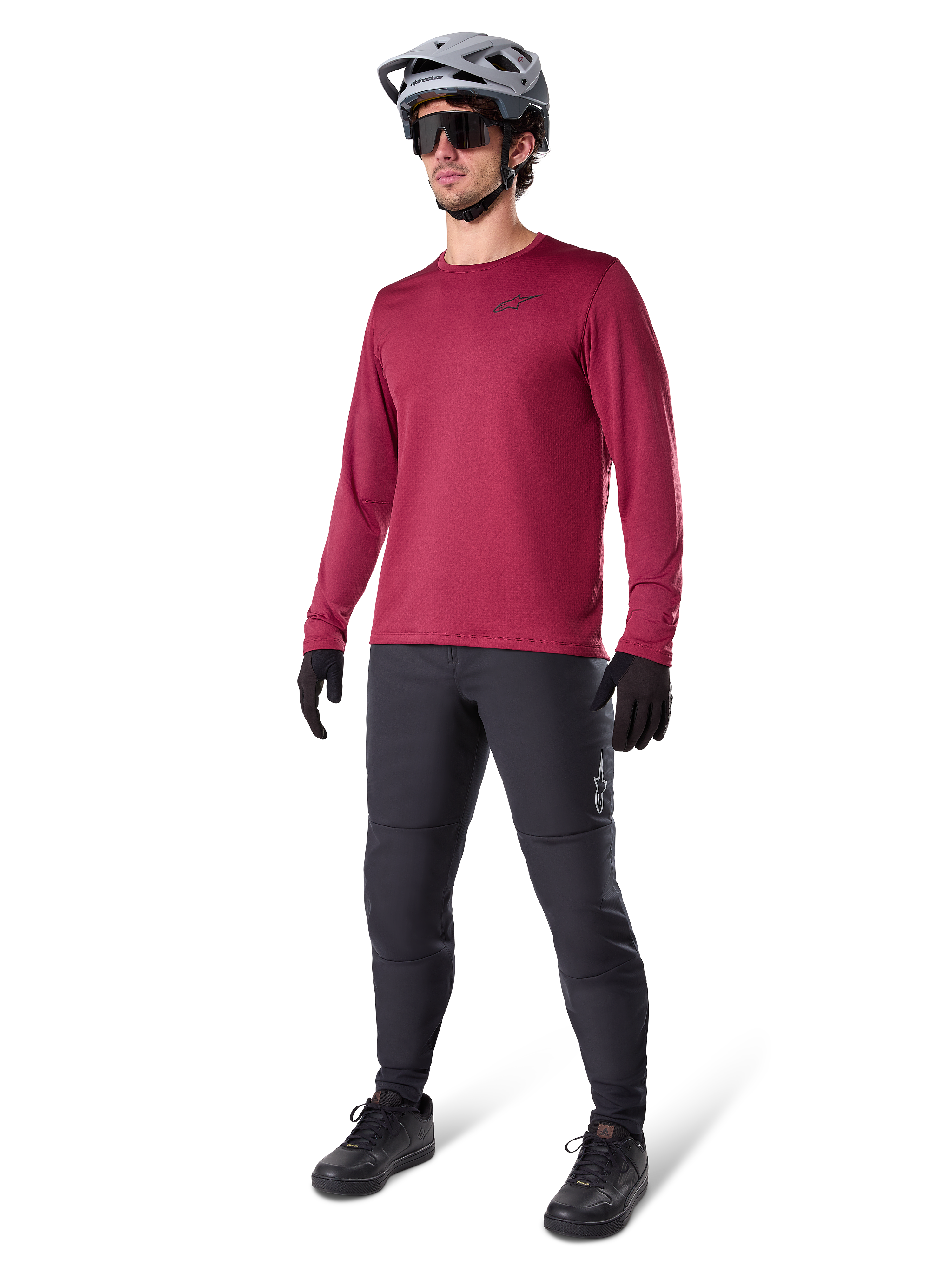 Alpinestars A-Dura Thermal Jersey w kolorze bordowym, ocieplana koszulka rowerowa z długim rękawem noszona z ciemnoszarymi spodniami MTB, czarnymi rękawiczkami i szarym kaskiem, ujęcie studyjne całej sylwetki odzieży rowerowej na zimne dni